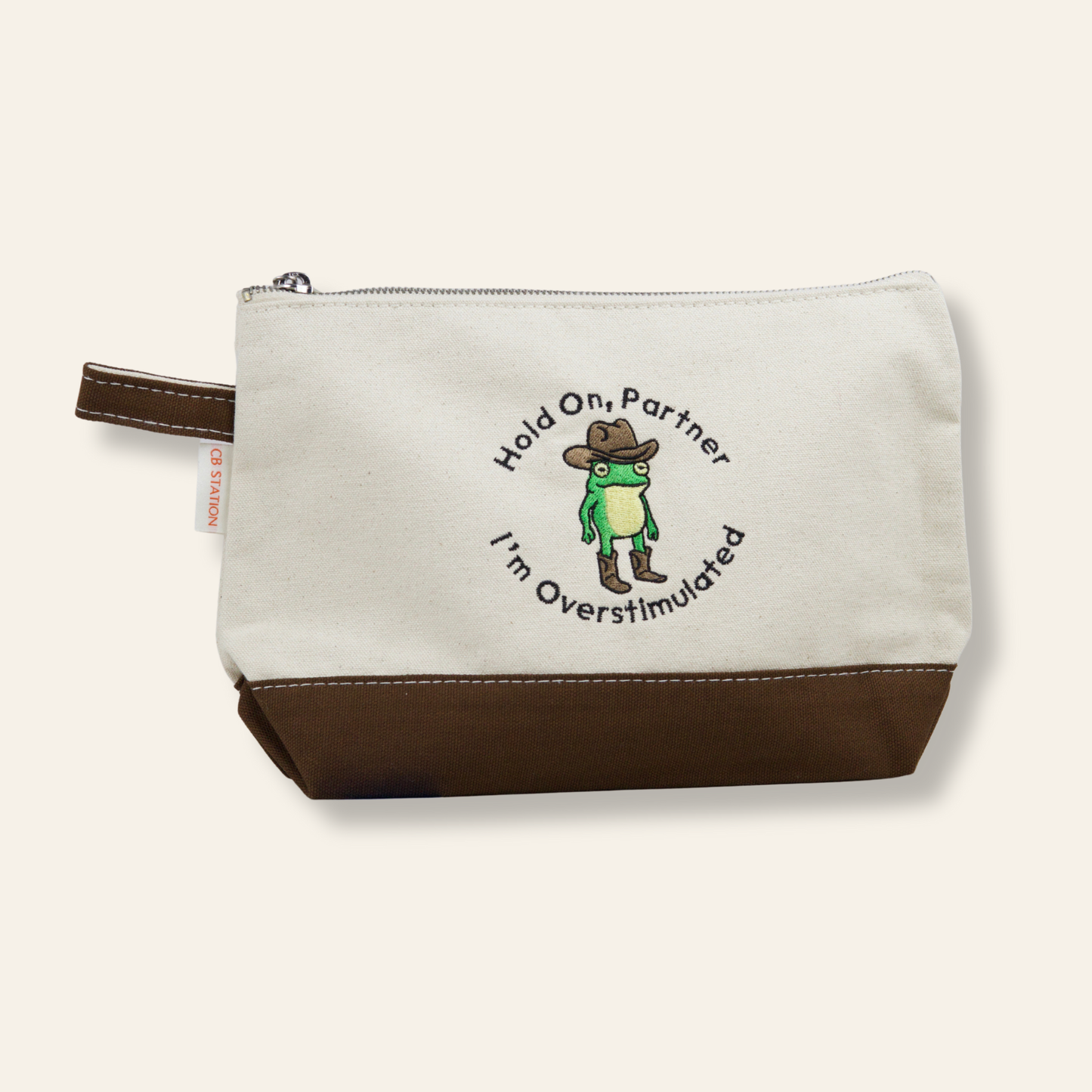 A funny embroidered canvas pouch featuring a cowboy frog and the phrase “Hold On, Partner — I’m Overstimulated.” Perfect for everyday organization and gifting.