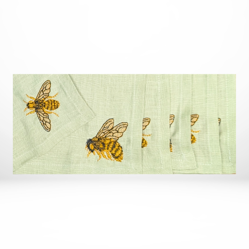 A set of light green fabric napkins embroidered with detailed golden honey bees in flight.