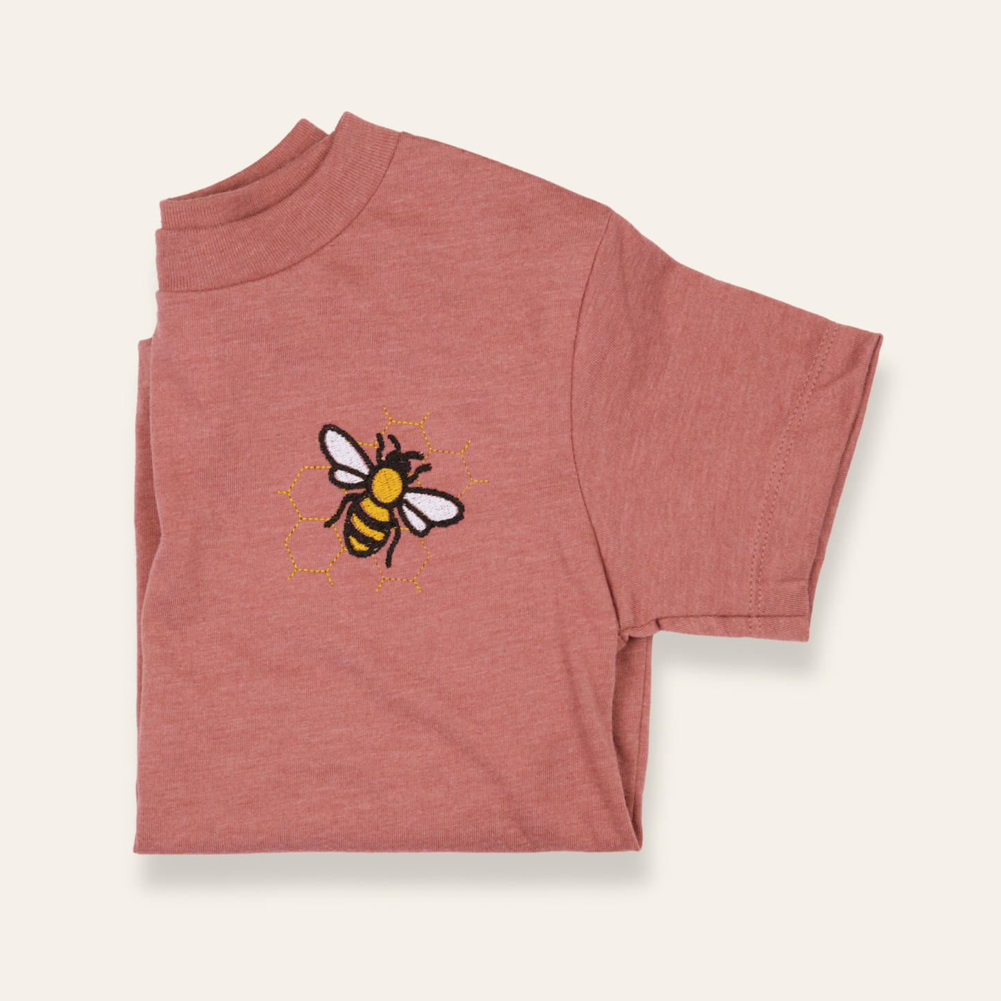 Dusty rose kids t-shirt featuring an embroidered bee with honeycomb detail. Soft, subtle, and perfect for everyday wear.