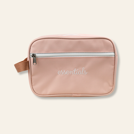 A blush travel pouch embroidered with “essentials.” Perfect for toiletries, makeup, and everyday organization at home or on the go.