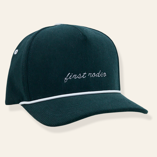 Forest green corduroy baseball cap featuring white script “girls rodeo” embroidery with contrast piping. Cool, confident, and easy to wear.