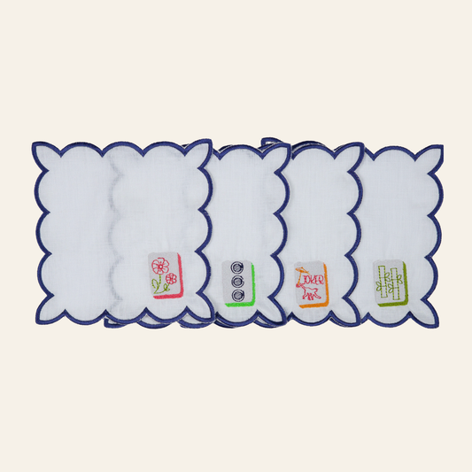 Set of four embroidered mahjong cocktail napkins with white fabric, navy scalloped edges, and colorful mahjong tile designs