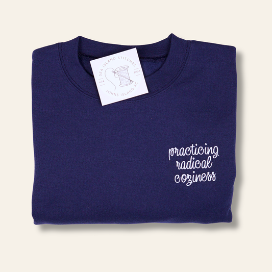 Embroidered navy sweatshirt with the phrase “Practicing Radical Coziness.” A soft, minimalist crewneck perfect for everyday wear, lounging, and gifting.