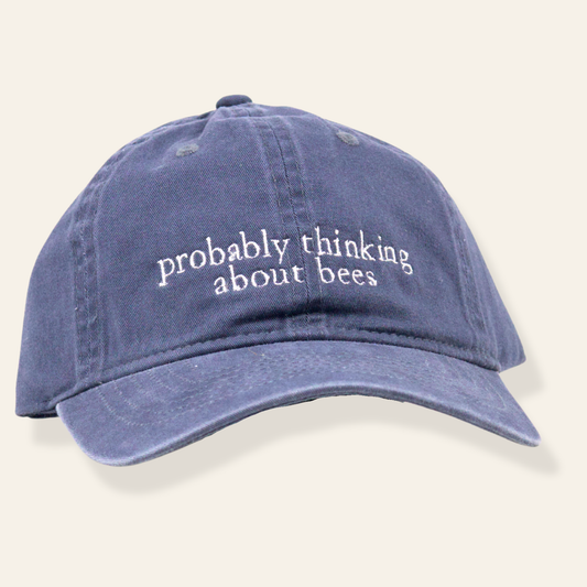 Washed navy embroidered cap featuring “probably thinking about bees.” Soft cotton, adjustable fit, and a thoughtful everyday accessory.