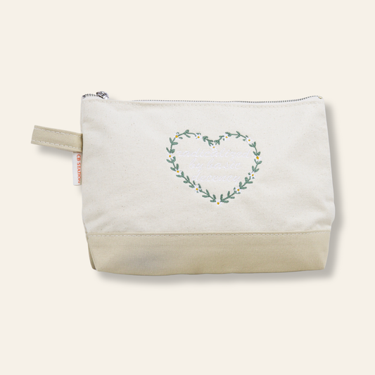 An embroidered canvas zipper pouch featuring the phrase “radicalized by basic human decency” inside a floral heart. Thoughtful, functional, and giftable.
