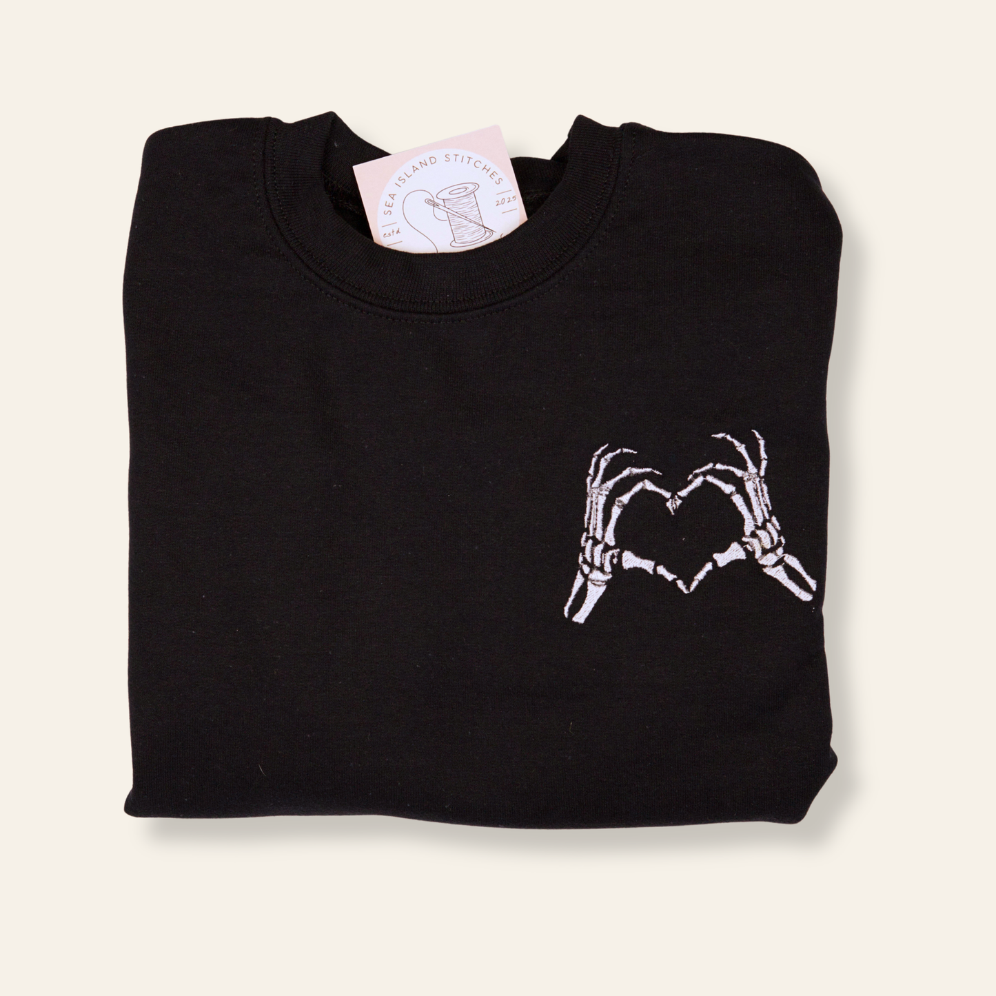 Black embroidered sweatshirt featuring skeleton hands forming a heart. Cozy, minimal, and perfect for spooky season or everyday wear.