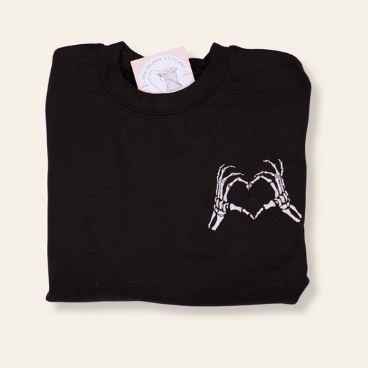 Black embroidered sweatshirt featuring skeleton hands forming a heart. Cozy, minimal, and perfect for spooky season or everyday wear.