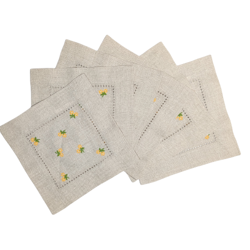 Set of six natural linen cocktail napkins with small embroidered yellow flower designs on a white background